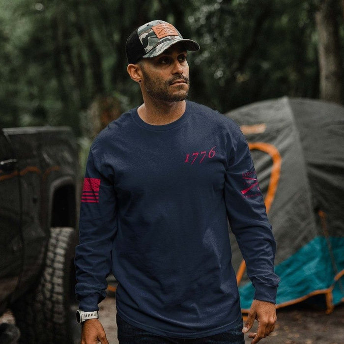 Man wearing a navy blue long-sleeve shirt with '1776' logo, standing in a camping area with tents and a vehicle.