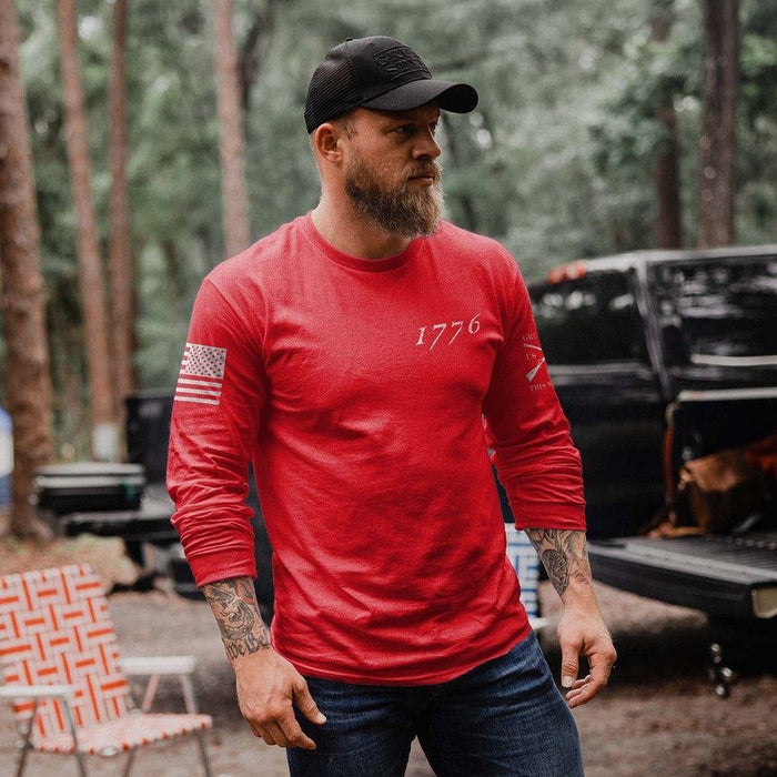 Man wearing a red long-sleeve shirt with '1776' and an American flag patch, standing outdoors.