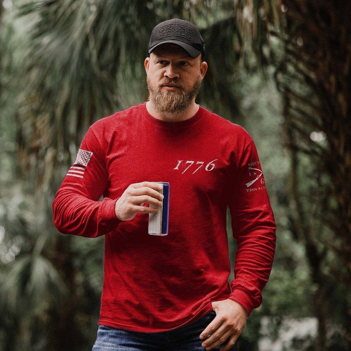Man wearing a red long-sleeve shirt with '1776' and a cap, holding a can, against a blurred natural background.