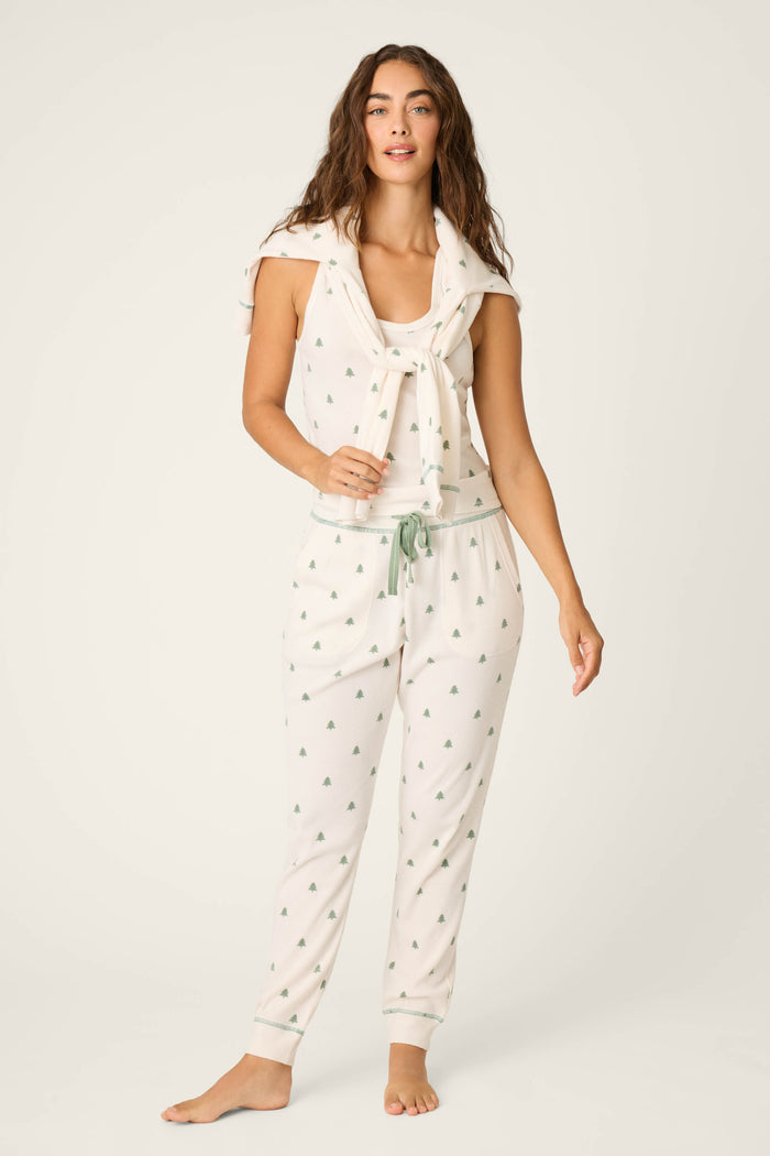 A woman stands barefoot against a plain background wearing the P.J. Salvage 4-Piece Tree Print Thermal Lounge Set, including a light-colored waffle pajama set with small green trees and a matching sweatshirt draped over her shoulders.