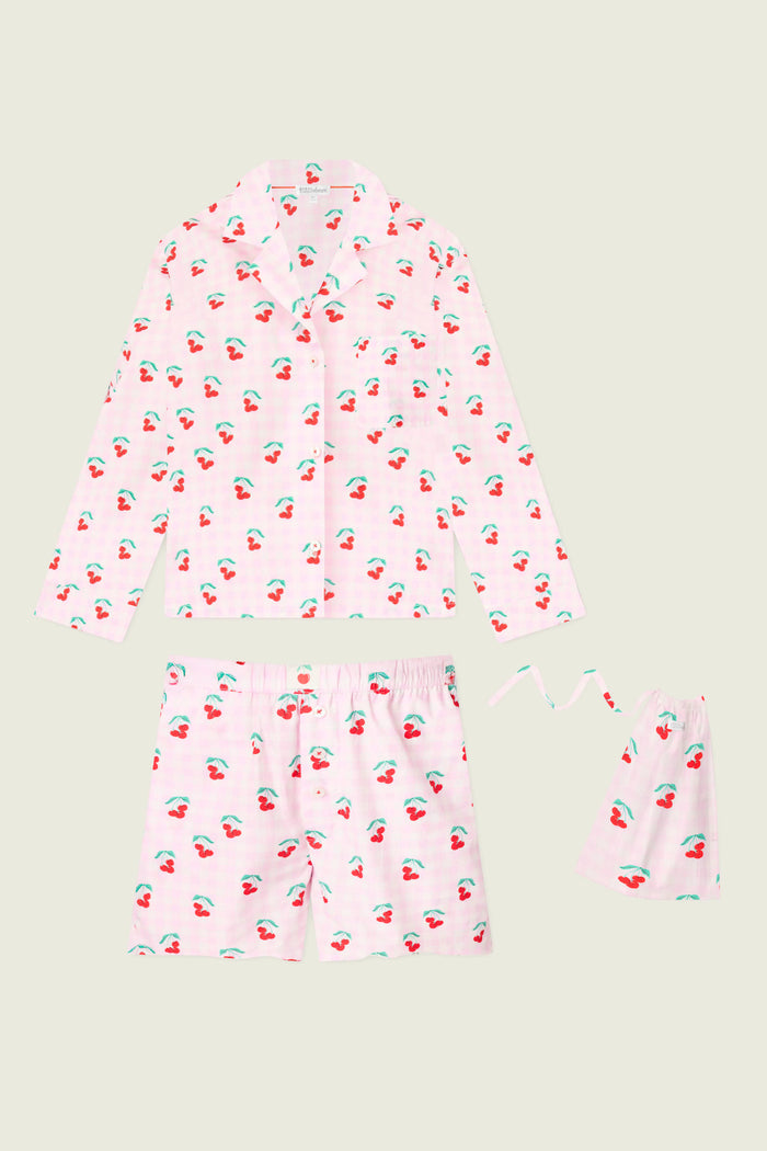 The P.J. Salvage Afterparty Poplin Oh Cherry Short PJ Set features a powder pink cotton poplin, cherry-printed long-sleeve button-up shirt, shorts, and a matching drawstring bag, all shown against a light background.