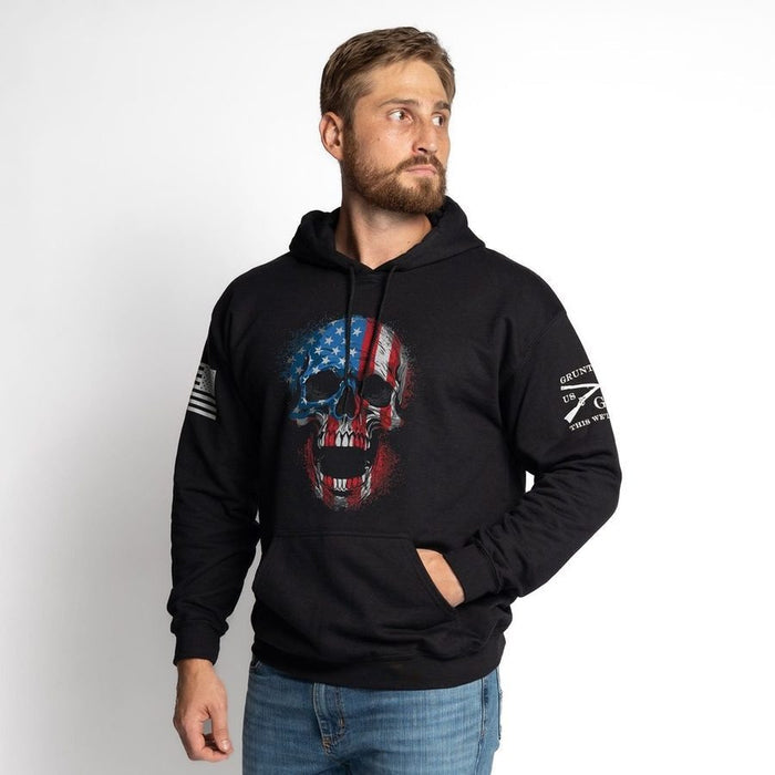 Man wearing a black hoodie with a skull design and American flag, standing against a white background.