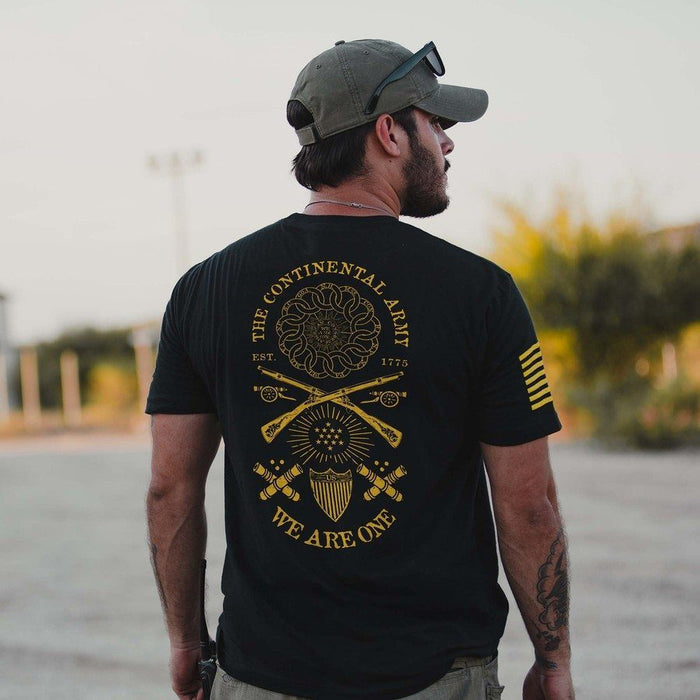 Man wearing a black t-shirt with yellow graphics and text, standing outdoors.
