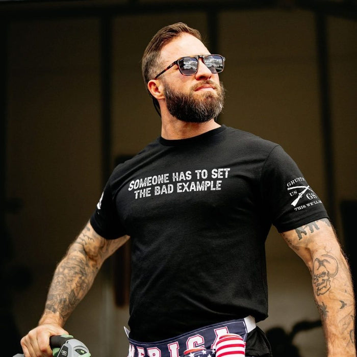 Man wearing a black t-shirt with text and sunglasses, standing outdoors.