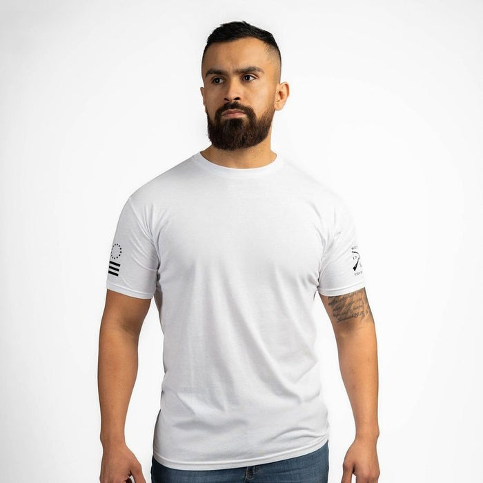 Man wearing a white t-shirt with logos on the sleeves against a plain background