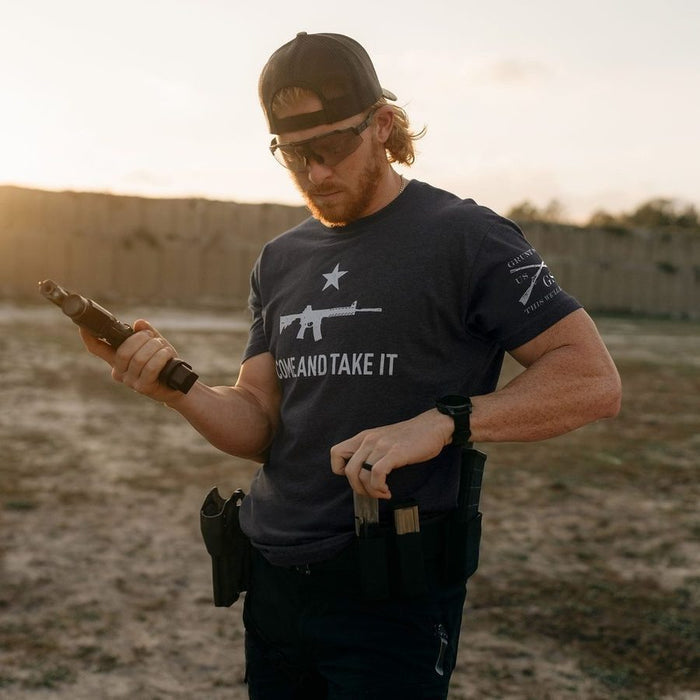 Man holding a rifle in an outdoor setting with a sunset in the background