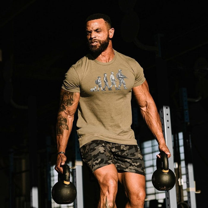 Man lifting kettlebells in a gym setting wearing a graphic t-shirt.
