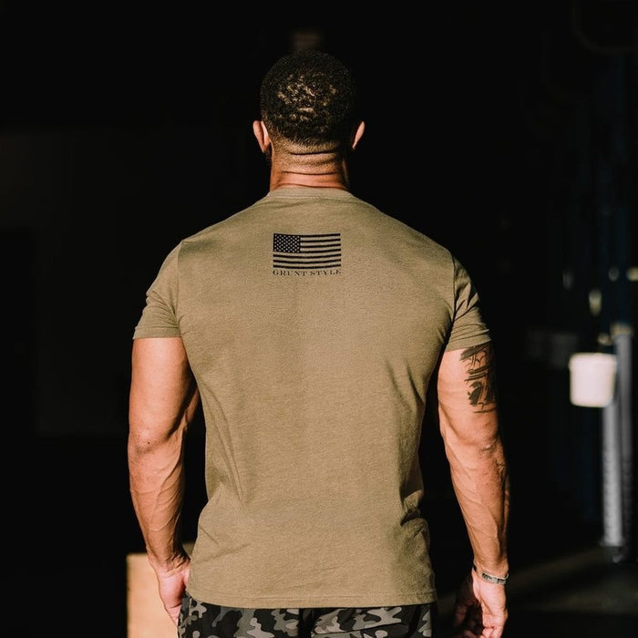 Man wearing a green t-shirt with an American flag design on the back, walking away in a dark setting.