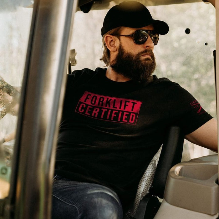 Man wearing a black t-shirt with 'Forklift Certified' text, sitting inside a vehicle.