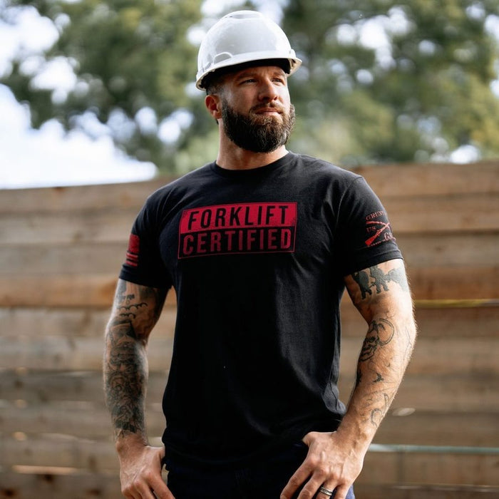 Man wearing a black 'Forklift Certified' t-shirt and white hard hat outdoors.