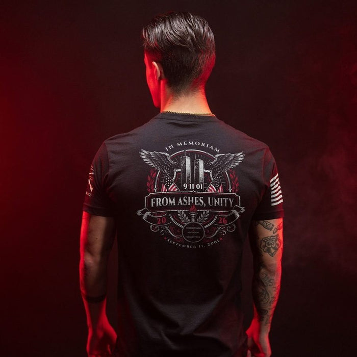 A man viewed from behind wearing a black graphic t-shirt with a large memorial design on the back reading 'FROM ASHES, UNITY' and 'IN MEMORIAM', set against a dark red background.