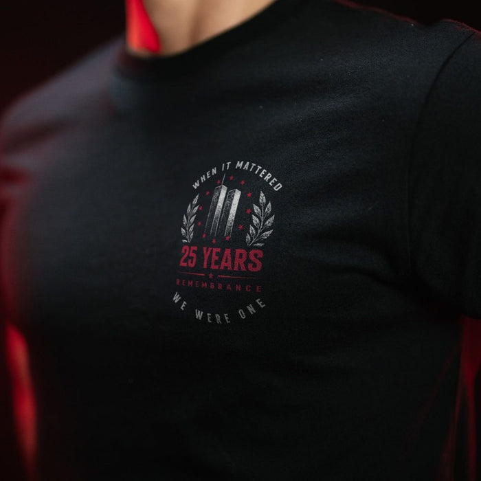 Close-up of a person wearing a black t-shirt with a red and gray graphic on the chest that reads '25 YEARS REMEMBRANCE WHEN IT MATTERED WE WERE ONE' with a stylized '11' emblem.