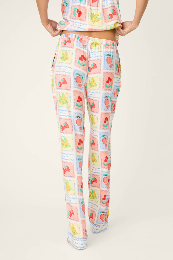 A person is shown from the back wearing P.J. Salvage Frutta Fresca Summer Harvest Open Leg Pants with a colorful fruit-print pattern; the matching top is partly visible against a plain, light background.
