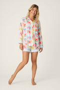 A woman poses barefoot, smiling in the P.J. Salvage Frutta Fresca Summer Harvest Short Lounge Set— a silky rayon sateen women’s pajama set with a multicolor fruit print, long-sleeve top, and matching shorts—adding playful charm to bedtime.