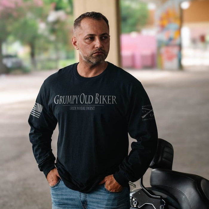 A man wearing a black long-sleeve t-shirt with 'Grumpy Old Biker' printed in white on the chest, standing next to a motorcycle in an outdoor setting.
