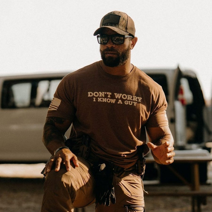 Man wearing a brown t-shirt with text, sitting in front of a vehicle.