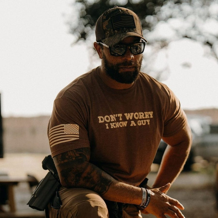 Man wearing a brown t-shirt with text and a cap, sitting outdoors.