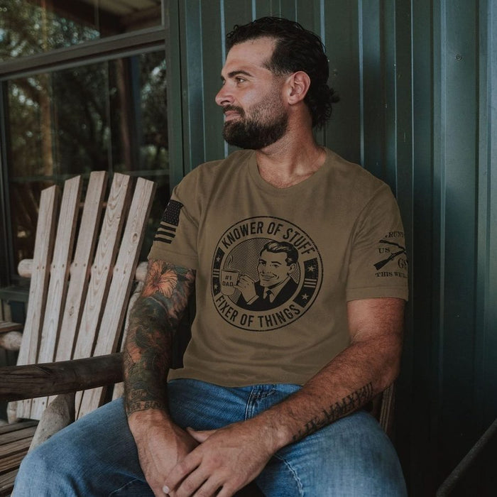 Man sitting on a wooden chair wearing a brown t-shirt with a graphic design.