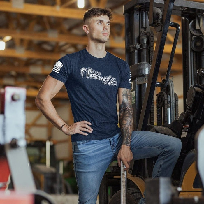 Man in a blue t-shirt and jeans standing next to a piece of industrial equipment in a warehouse.