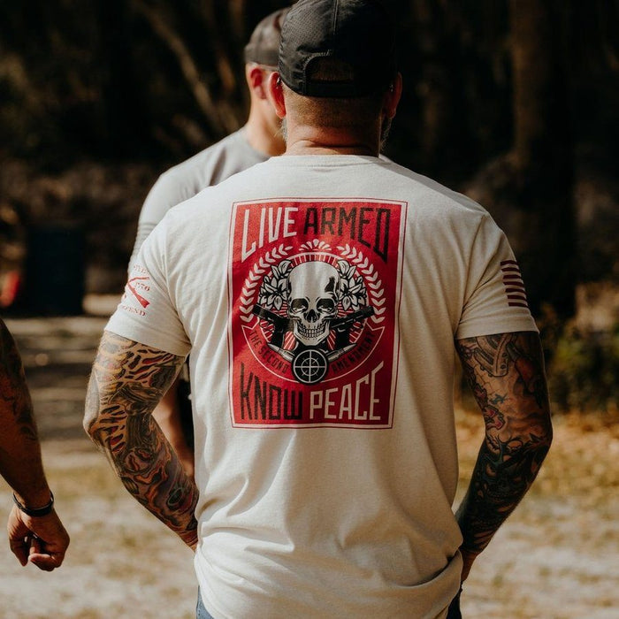 Person wearing a white t-shirt with a graphic design and text on the back, standing outdoors.