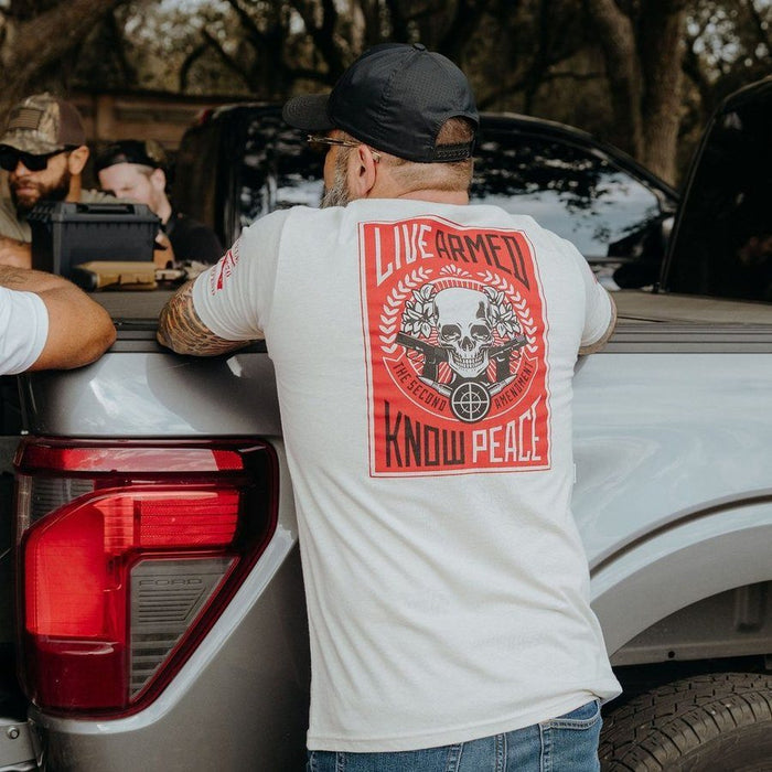 Man wearing a white t-shirt with a red graphic design, standing next to a vehicle.
