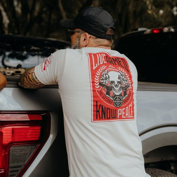 Man wearing a white t-shirt with a red graphic design, leaning against a vehicle.