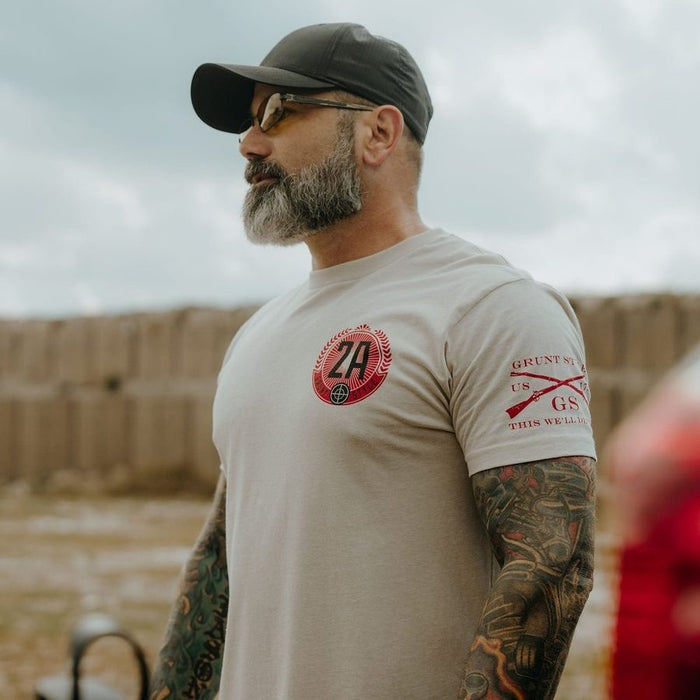 Man wearing a beige t-shirt with graphics and text, standing outdoors.