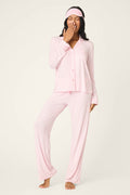 A person stands barefoot against a plain light background, wearing the P.J. Salvage Modal Basics Pink Stripe 3-Piece PJ Set and matching sleep mask, covering their mouth as if yawning.