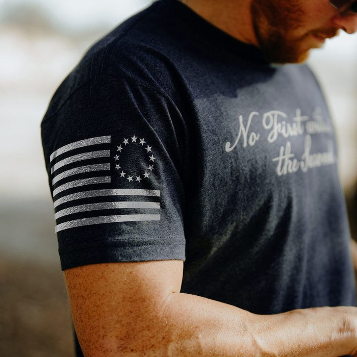 Person wearing a dark t-shirt with a flag design and text on the sleeve and chest.