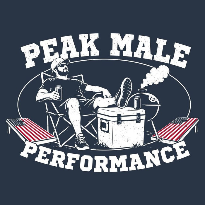 A dark navy graphic print featuring a white distressed illustration of a man relaxing in a folding chair with his feet up on a cooler, surrounded by a grill, lounge chairs with American flags, and the text 'PEAK MALE PERFORMANCE'.