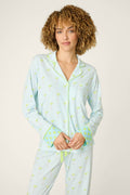 A person with curly hair wears the P.J. Salvage Playful Prints Salty Cadillac Long Sleeve Top, a soft cotton-modal jersey pajama shirt with light blue and white stripes, green patterns, and polka-dot cuffs, against an off-white background.