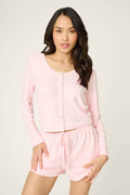 A woman with long dark hair wears the P.J. Salvage Pointelle Essentials Ballet Pink Cardigan, standing against a light background, facing forward with one hand on her hip.