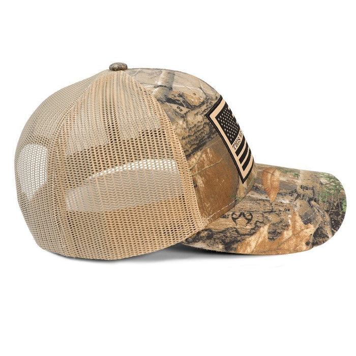 A trucker-style baseball cap with a tan mesh back and a camouflage front panel and brim, featuring a black-and-tan American flag patch on the side.