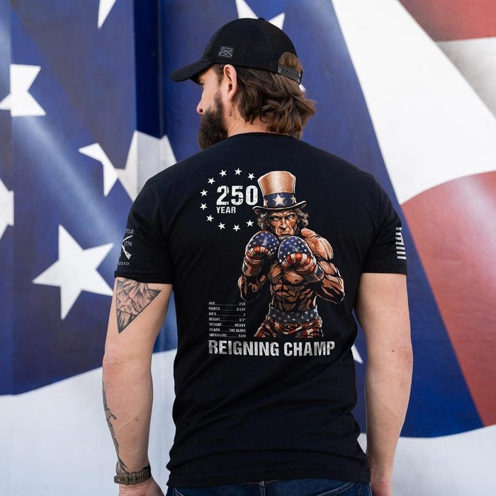 Person wearing a black t-shirt with a graphic design in front of an American flag.