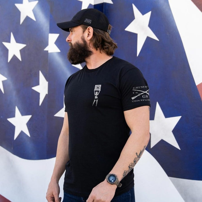 Man wearing a black t-shirt with logos in front of an American flag