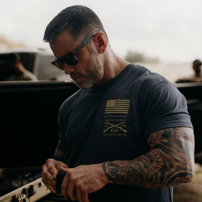 Man wearing sunglasses and a black t-shirt with a logo, working on something outdoors.