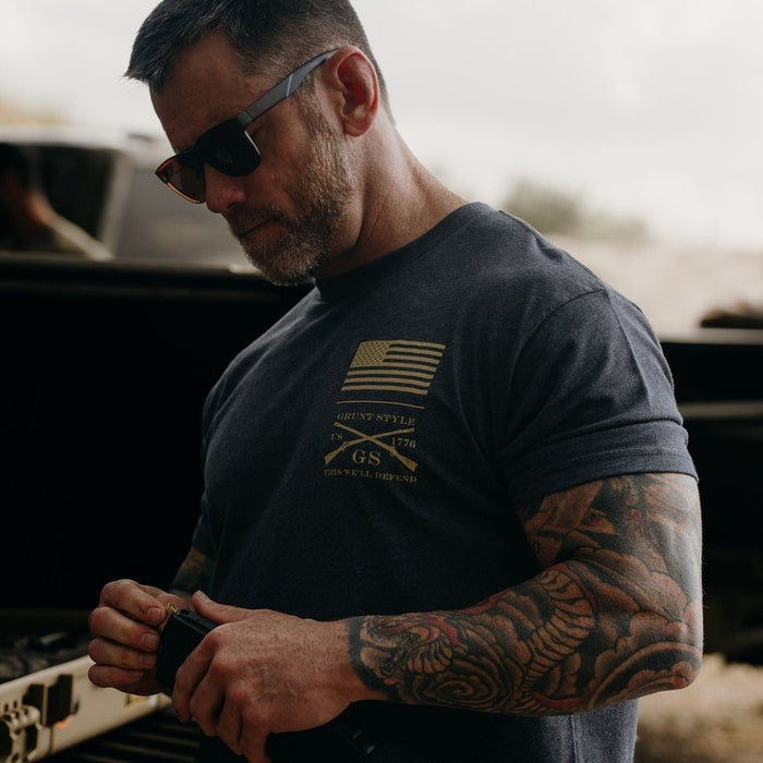 Man wearing sunglasses and a black t-shirt with a logo, standing next to a vehicle.