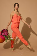 A woman walks barefoot on a beige background, holding a colorful basket filled with pink flowers and greenery.