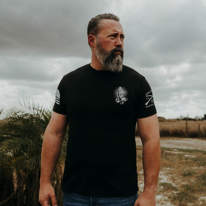 Man wearing a black t-shirt with a logo outdoors on a cloudy day