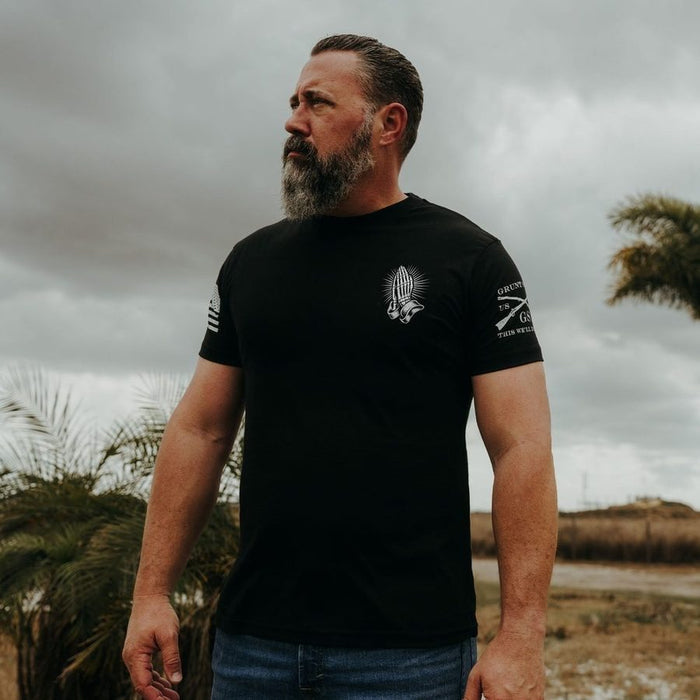 Man wearing a black t-shirt with a logo and text outdoors on a cloudy day