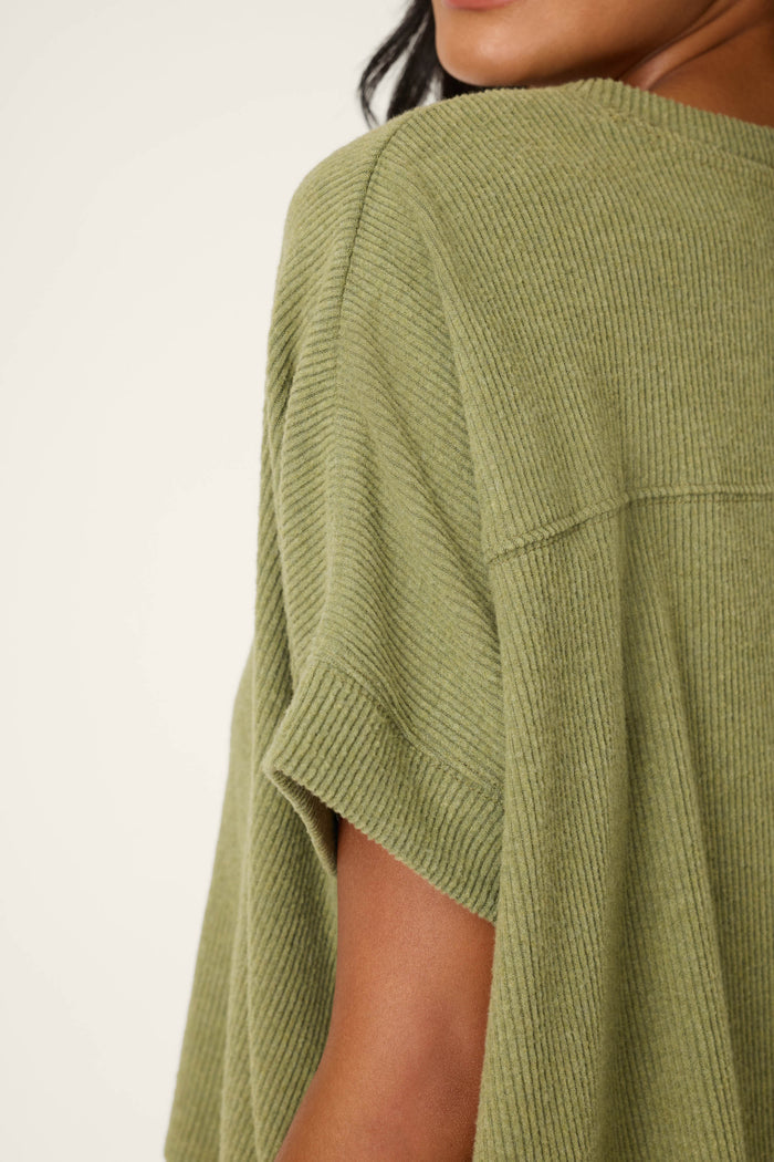 Close-up of a person in the P.J. Salvage Olive You Forever Lounge Set, featuring a loose, short-sleeved, ribbed olive green top. Only part of their face, shoulder, and upper arm is shown against a plain light background.