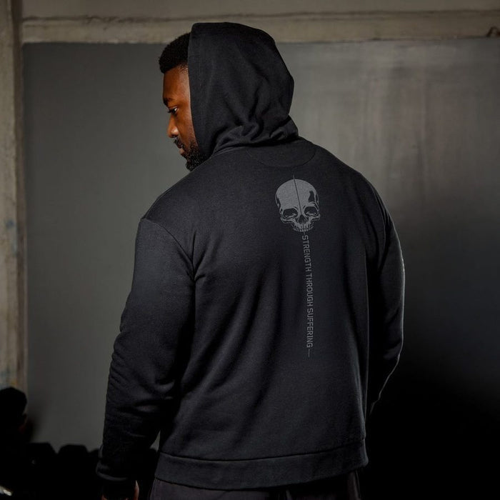 Person wearing a black hoodie with a skull design on the back, standing in a dimly lit room.