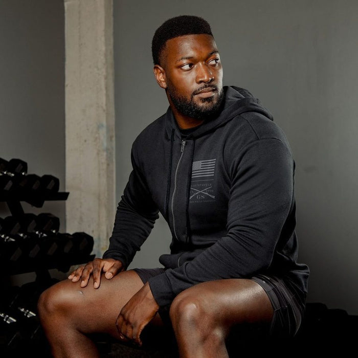 Man in black hoodie sitting in a gym setting with weights in the background
