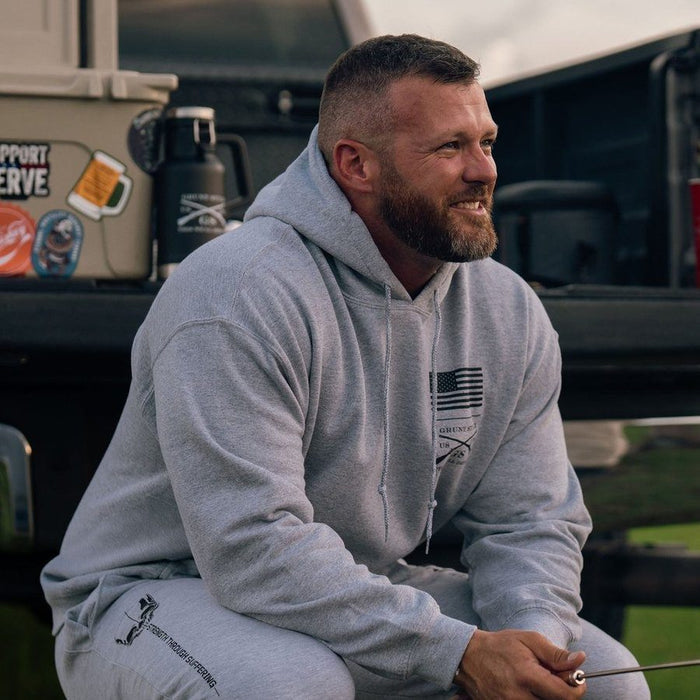 Man in a gray hoodie sitting outdoors with a vehicle in the background