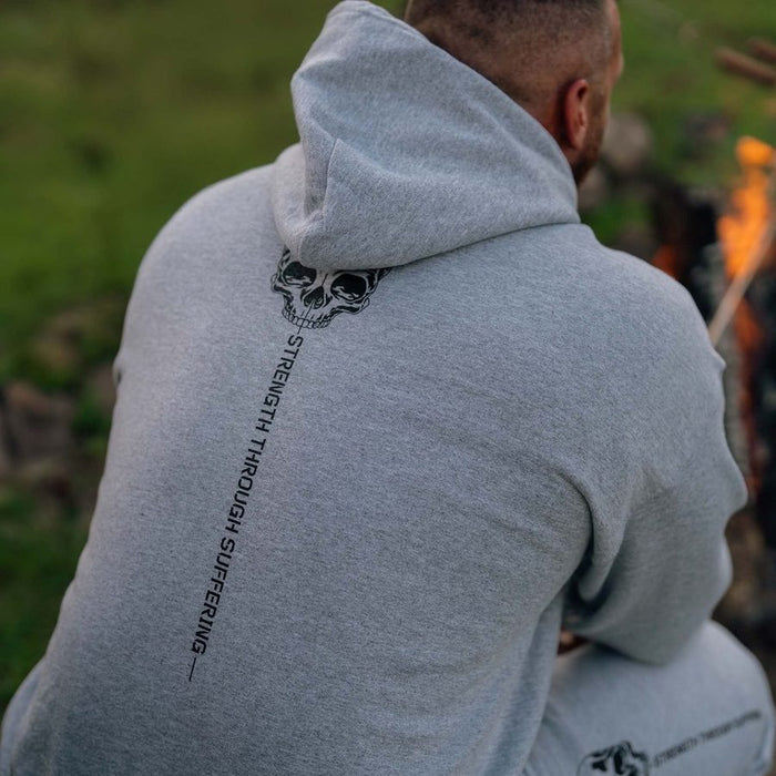 Person wearing a gray hoodie with a skull design and text on the back, sitting by a campfire.