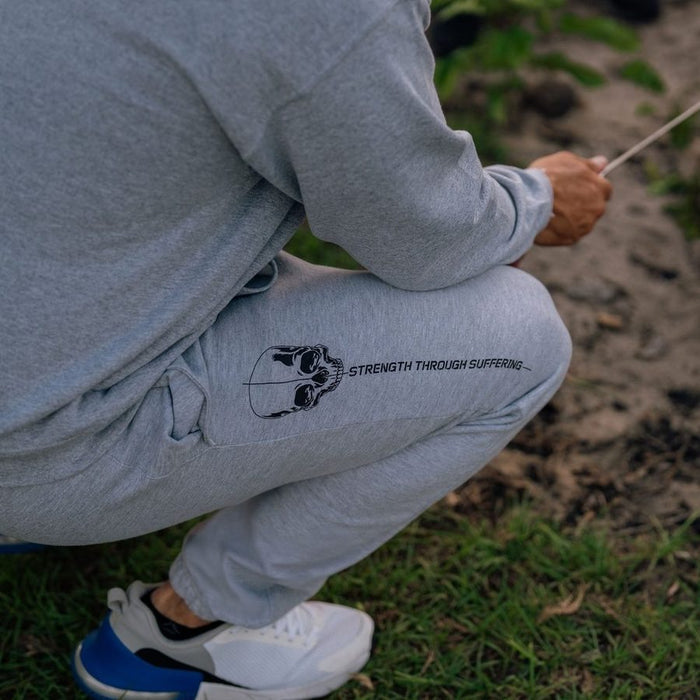 Person wearing gray sweatpants with 'Strength Through Suffering' text, crouching outdoors.