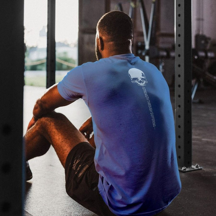 Person sitting on the floor in a gym wearing a blue t-shirt with a skull design.