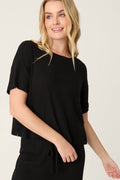 A person with long blonde hair wears the P.J. Salvage Textured Essentials Black Short Sleeve Top and a matching drawstring skirt, standing against a plain light background and smiling slightly.