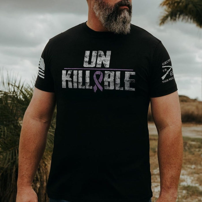 Man wearing a black t-shirt with 'UNKILLABLE' text and purple ribbon design outdoors.