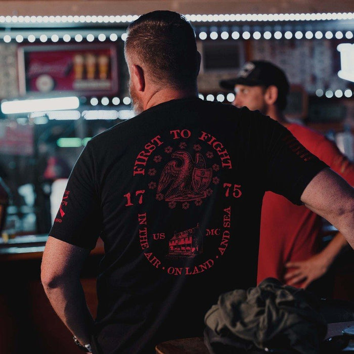 Man wearing a black t-shirt with red text and graphics in a bar setting